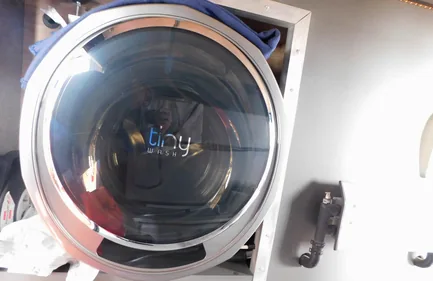 Frontansicht einer nachgerüsteten Tinywash Waschmaschine im Wohnmobil mit sichtbaren Einbaukomponenten